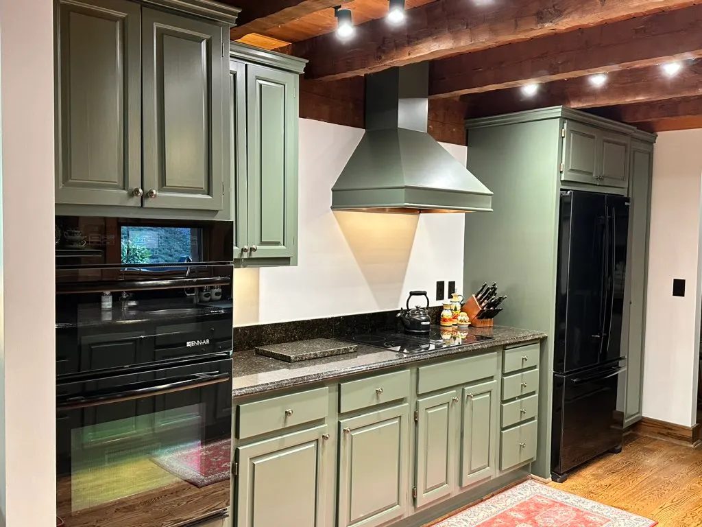 Green painted kitchen cabinetry with dark beams
